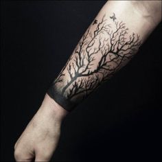 a person's arm with a tree and bird tattoo on the left side of their arm