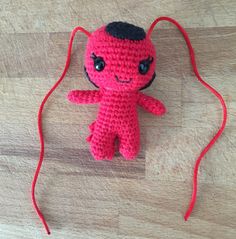 a red crocheted stuffed animal sitting on top of a wooden floor next to a string