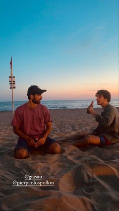 two men sitting in the sand talking to each other on the beach at sunset or sunrise