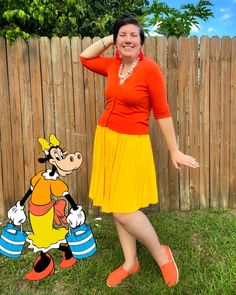 a woman standing in front of a wooden fence wearing an orange top and yellow skirt