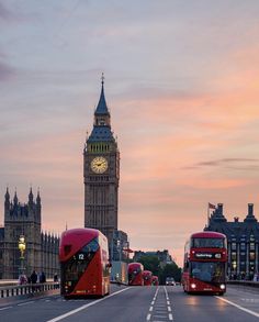 two red double decker buses driving down the street in front of big ben at sunset