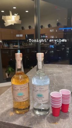 two bottles of alcohol sitting on top of a counter next to some cups and glasses