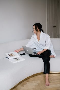 a woman sitting on top of a white couch with a laptop computer in her lap