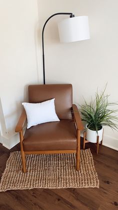 a brown chair sitting next to a lamp on top of a wooden floor with a white pillow