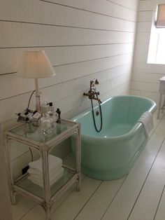 a bath tub sitting next to a table with a lamp on it's side