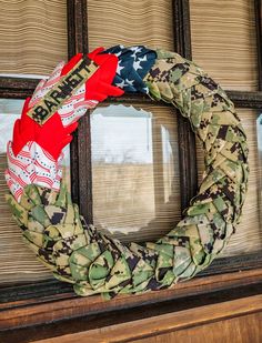 a camouflage wreath with red, white and blue ribbons hanging on a window sill