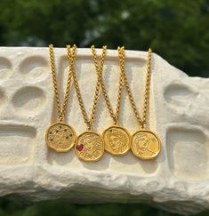 four gold coin necklaces sitting on top of a white stone slab with trees in the background