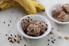 two white bowls filled with ice cream and chocolate chips next to bananas on a table