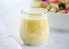 a glass jar filled with dressing next to a bowl of salad