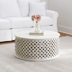 a white coffee table with flowers on top in front of a couch and rugs