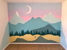 an empty room with mountains painted on the wall and wood flooring in front of it