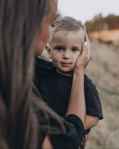 a woman holding a little boy in her arms while he looks at the other side