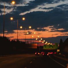 cars driving down the road at night with street lights in the distance and clouds in the sky