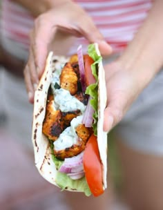 a person holding a taco with chicken, lettuce and tomatoes