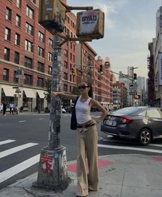 a woman standing next to a traffic light on the side of a road with buildings in the background