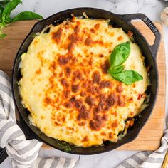 a skillet filled with cheese and spinach on top of a wooden cutting board