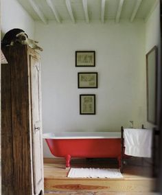 a bathroom with a red bathtub and pictures on the wall above it, along with a white rug