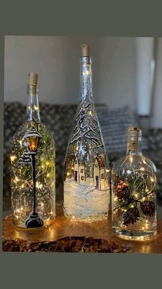 three wine bottles with lights in them sitting on a table next to a piece of wood