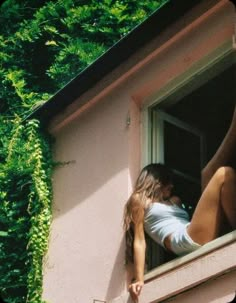 a woman leaning out the window of a pink building with ivy growing on it's side