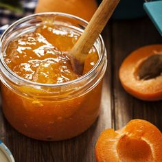 a jar filled with orange marmalade sitting on top of a wooden table next to sliced peaches