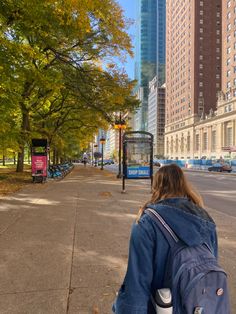 a woman walking down the street with a backpack on her back and buildings in the background