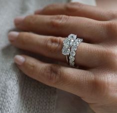 a woman's hand with a diamond ring on top of her finger and the other hand holding an engagement ring