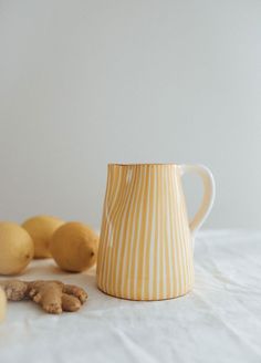 a yellow and white striped coffee mug next to lemons on a white tablecloth