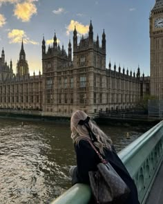 a woman standing on the edge of a bridge looking at big ben in london, england