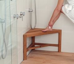 a person standing over a wooden bench in a bathroom next to a walk in shower