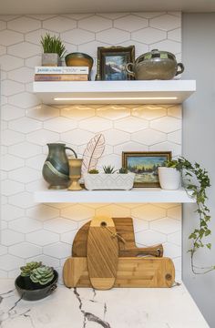 two shelves with plants and other items on them in a white kitchen, one shelf has a wooden cutting board