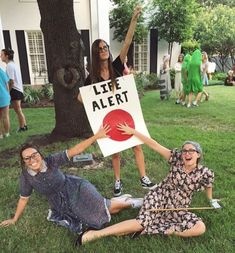 three people sitting on the grass holding up a sign that says, little alert with two women behind them