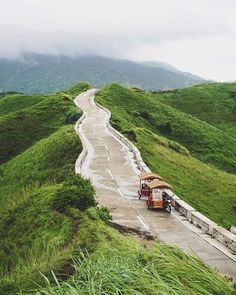 an orange truck driving down a road next to lush green hills