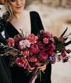 a man holding a bouquet of flowers next to a woman in a black dress and leather jacket