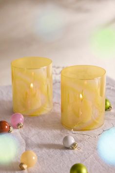 two yellow candles sitting next to each other on a white tablecloth with ornaments around it