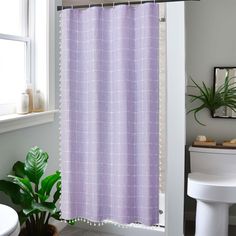 a white toilet sitting next to a bath tub under a bathroom window with a purple shower curtain