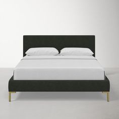 a bed with white sheets and black headboard in front of a plain wall background