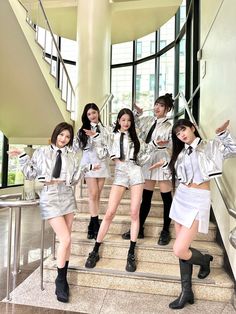 the girls are posing on the stairs in their silver outfits and black boots, all wearing short skirts