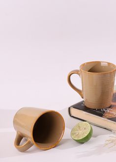 a coffee cup sitting on top of a book next to a slice of kiwi