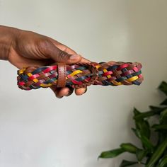 a hand holding a multicolored leather bracelet in front of a potted plant