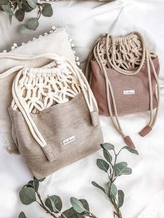 two purses sitting on top of a bed next to some green leaves and branches