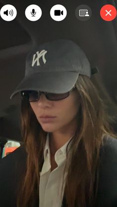 a woman wearing a yankees hat and sunglasses in the back seat of a car while looking at her cell phone