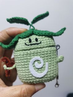 a hand holding a crocheted green bag with a smiling face on it's side