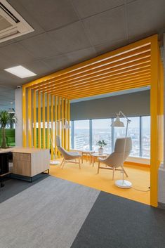 an office with yellow and grey walls, chairs and desks in the foreground