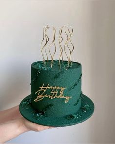 a person holding a green cake with gold decorations on it and the words happy birthday written on top