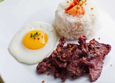 a white plate topped with rice and meat next to an egg on top of it