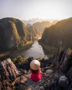 a woman sitting on top of a mountain next to a lake