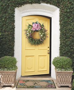 a yellow door with a wreath on it and two planters in front of it