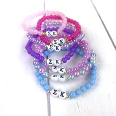 four bracelets with beads and letters on them sitting on a white surface, one is for the letter k