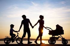 two adults and a child holding hands as the sun sets behind them with a baby in a stroller