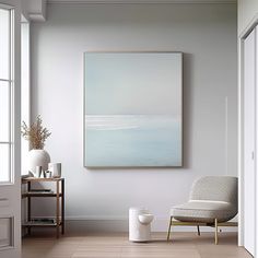 a painting hangs on the wall above a chair in a room with white walls and wooden floors